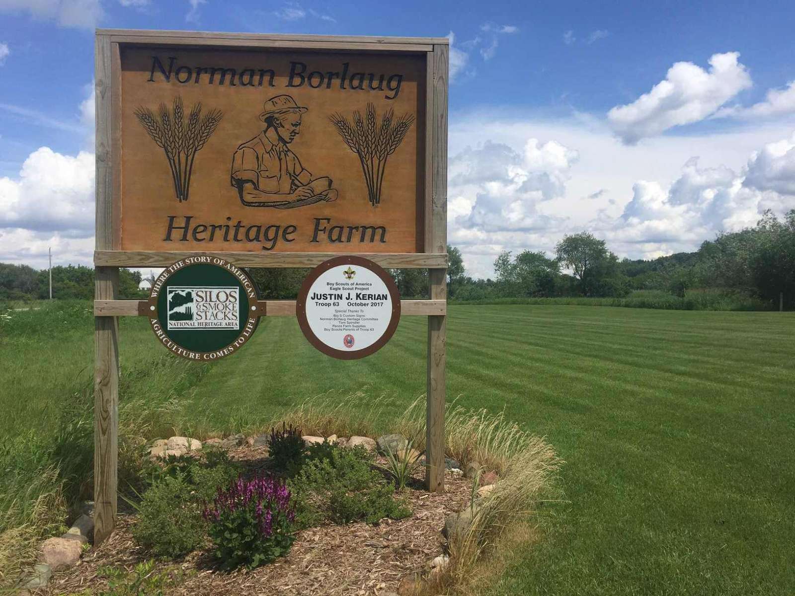 Wooden sign in green field reading Norman Borlaug Heritage Farm